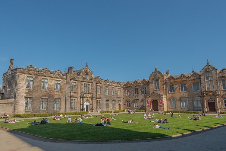 Students sit on a lawn in front of old University buildings
