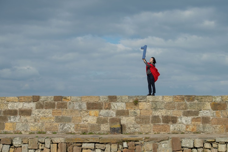 Student holding number 1 while standing on the Long Pier in St Andrews