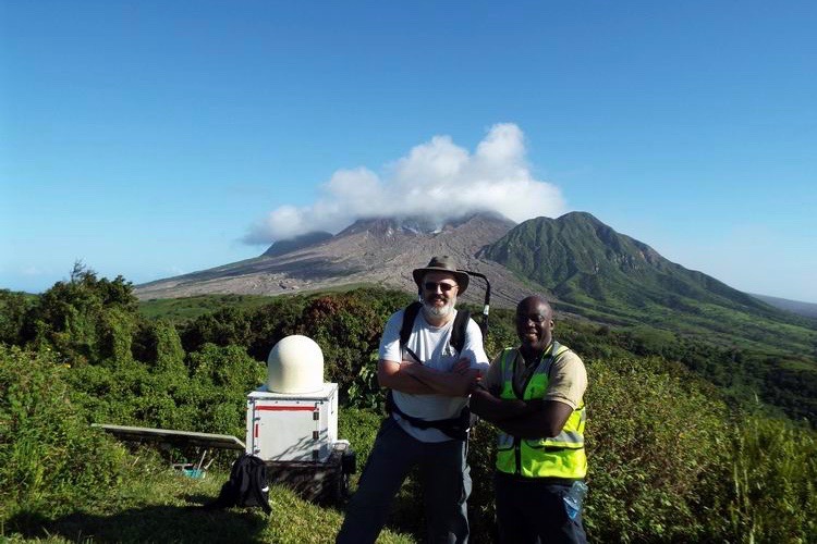 Two men standing besides the radar with a volcano in the background.