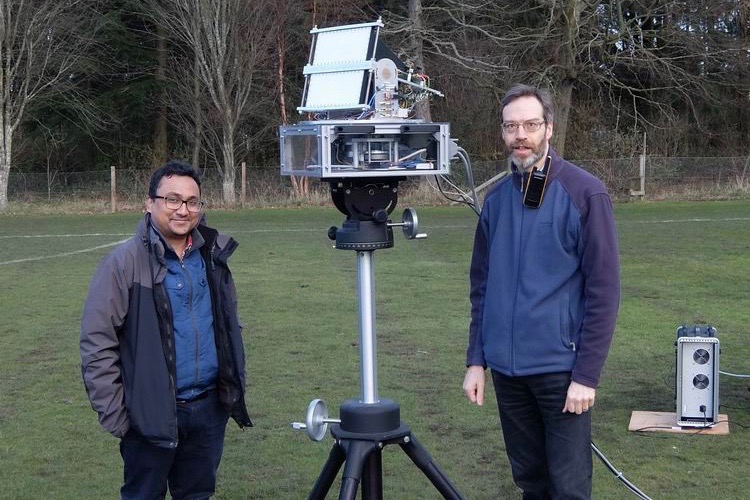 Two scientists standing outside with a radar monted in a tripod.
